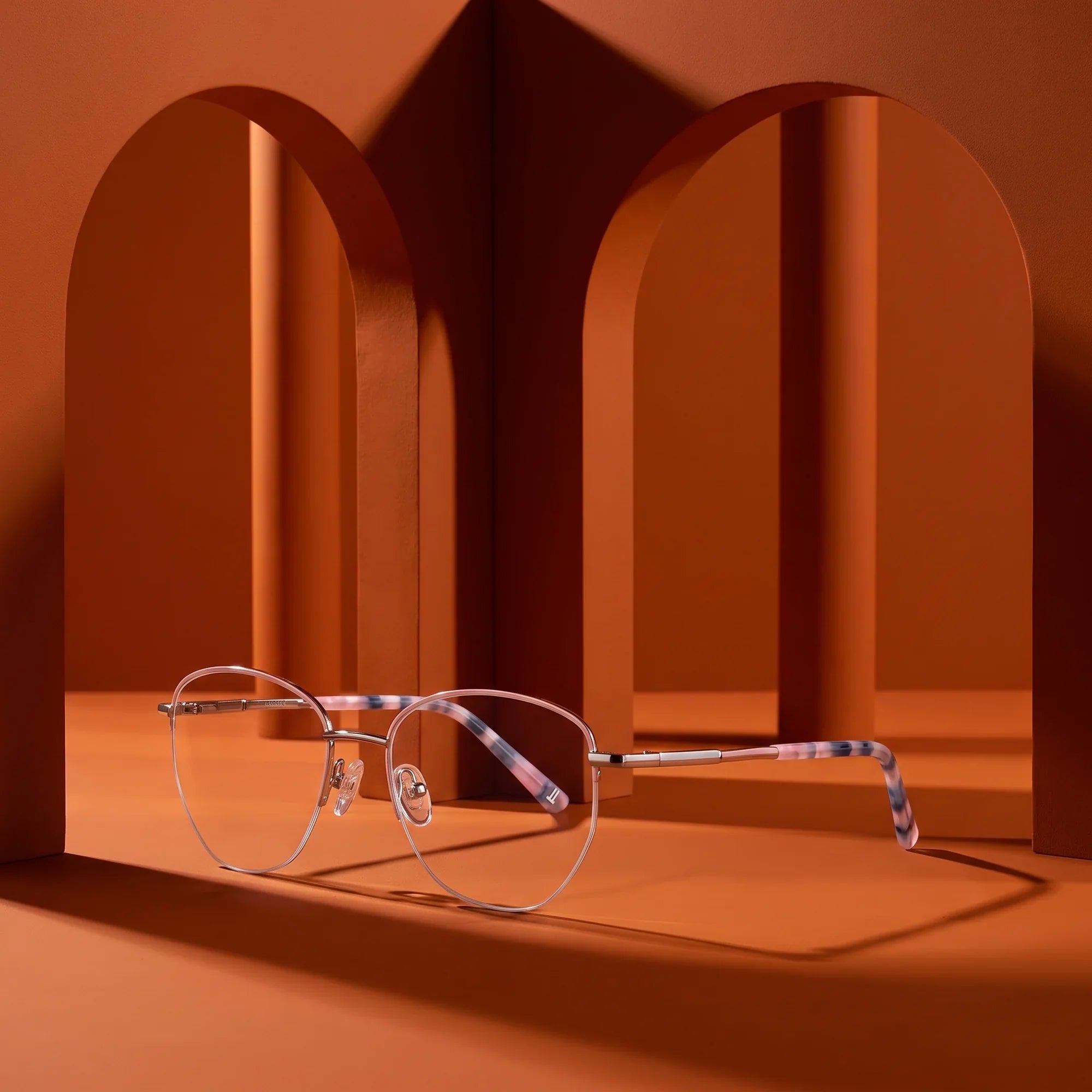 Anteojos Fiore 3921 en pink silver – displayed on a burnt orange podium among arches