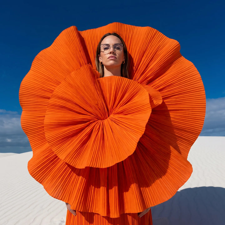 Anteojos Fiore 3971 en black gold, en modelo – retrato de campaña, abanico plisado naranja escultórico sobre dunas blancas