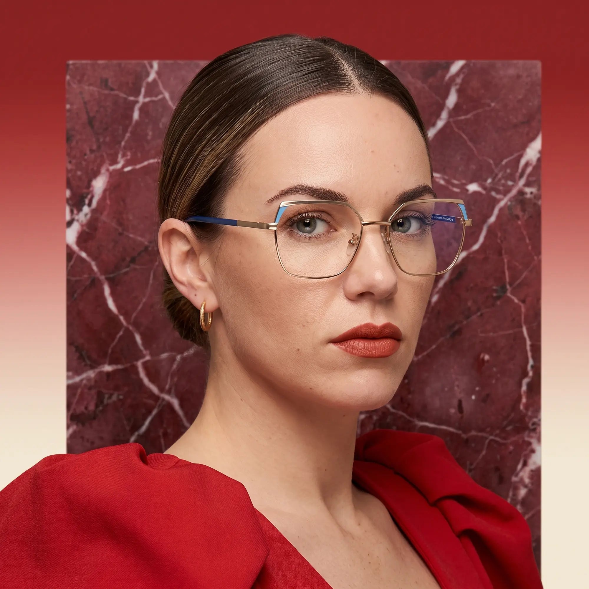 Anteojos Fiore 3971 en grey gold, en modelo – retrato de campaña, fondo de mármol rojo y vestido escarlata drapeado