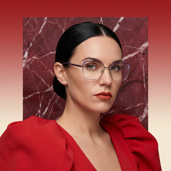 Anteojos Fiore 3971 en purple silver, en modelo – retrato de campaña, fondo de mármol rojo y vestido escarlata drapeado