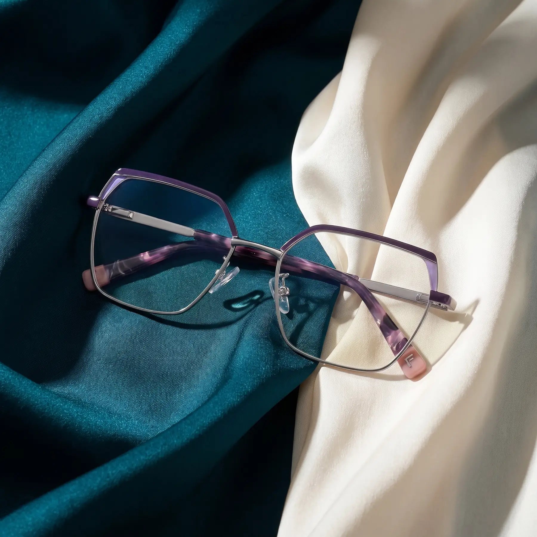 Anteojos Fiore 3971 en purple silver – resting on draped teal and ivory silk