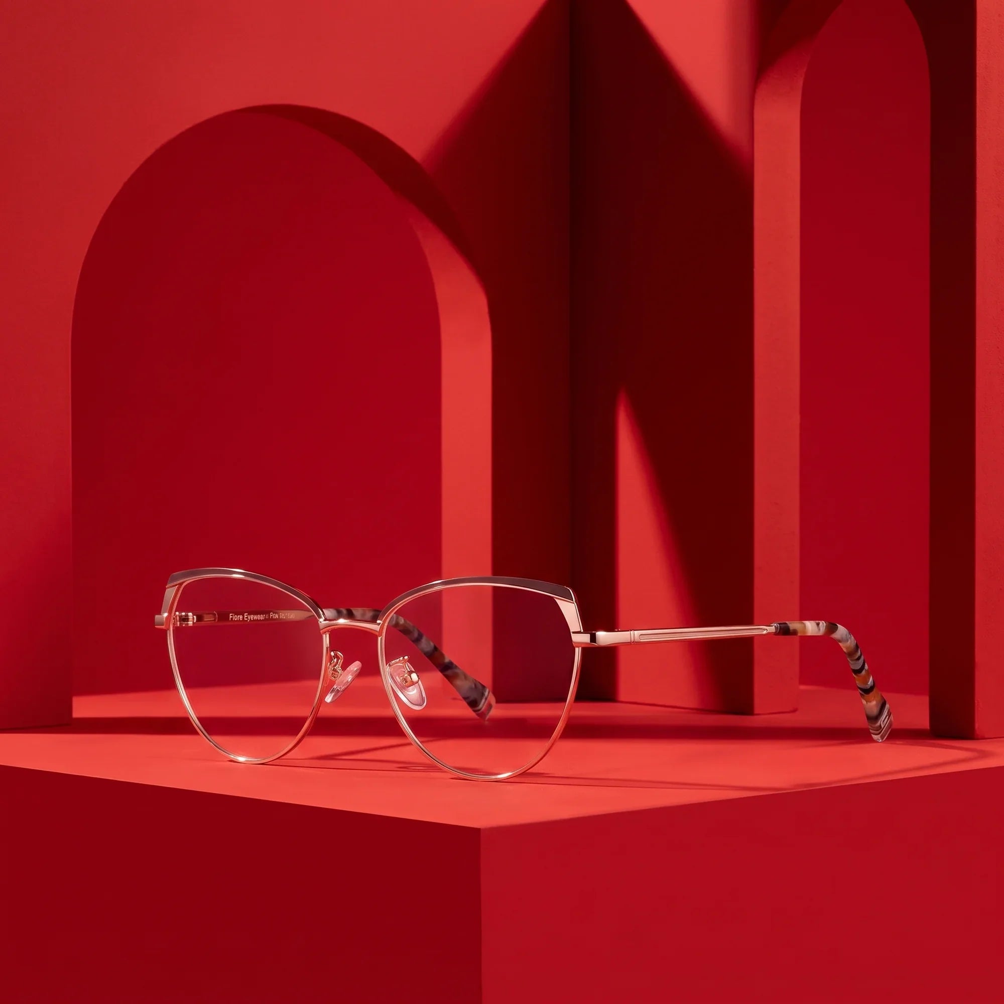 Anteojos Fiore 3983 en brown gold – staged on a sculptural vivid red architecture set