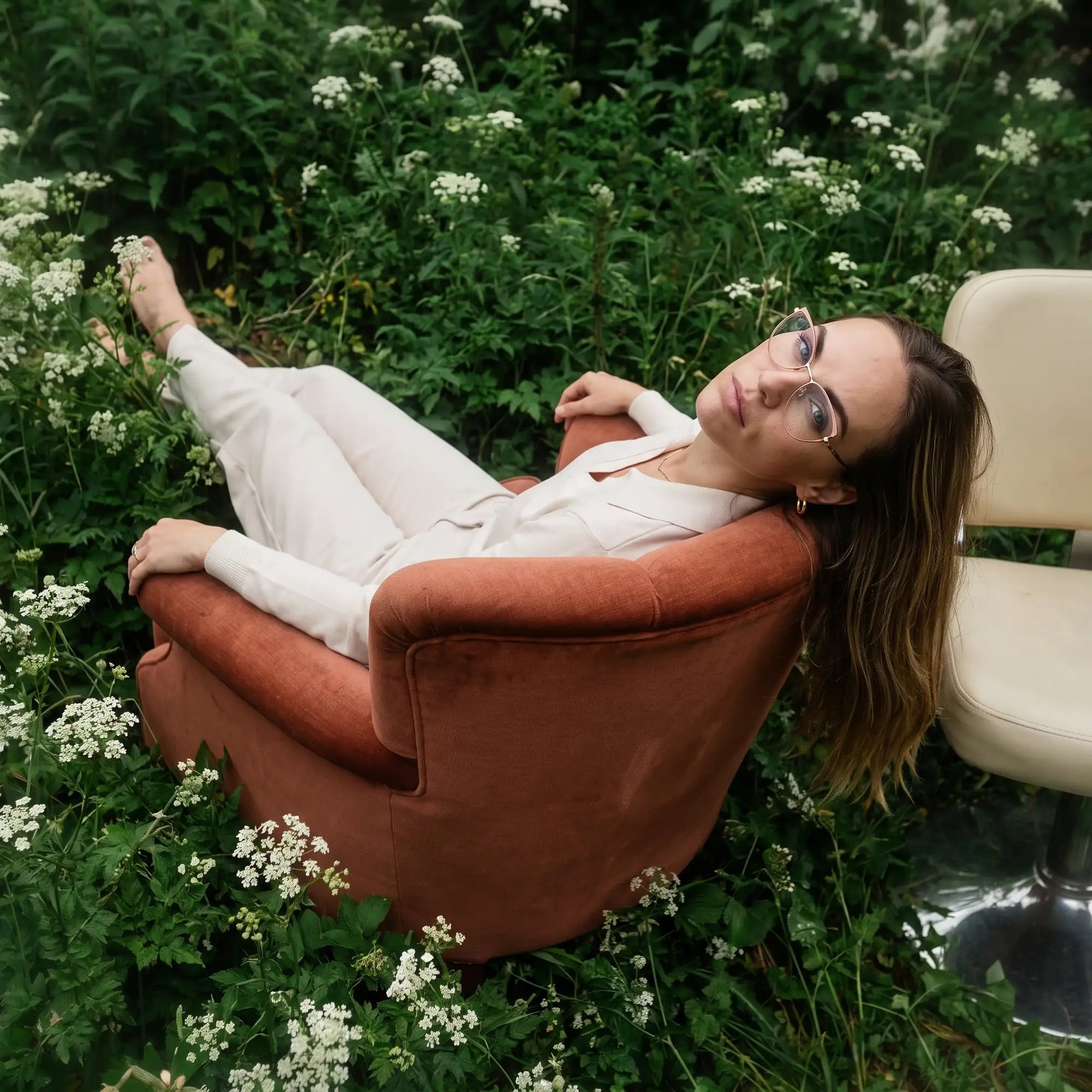 Anteojos Fiore 3983 en pink gold, en modelo – retrato de campaña, lounging in an armchair in a wildflower meadow