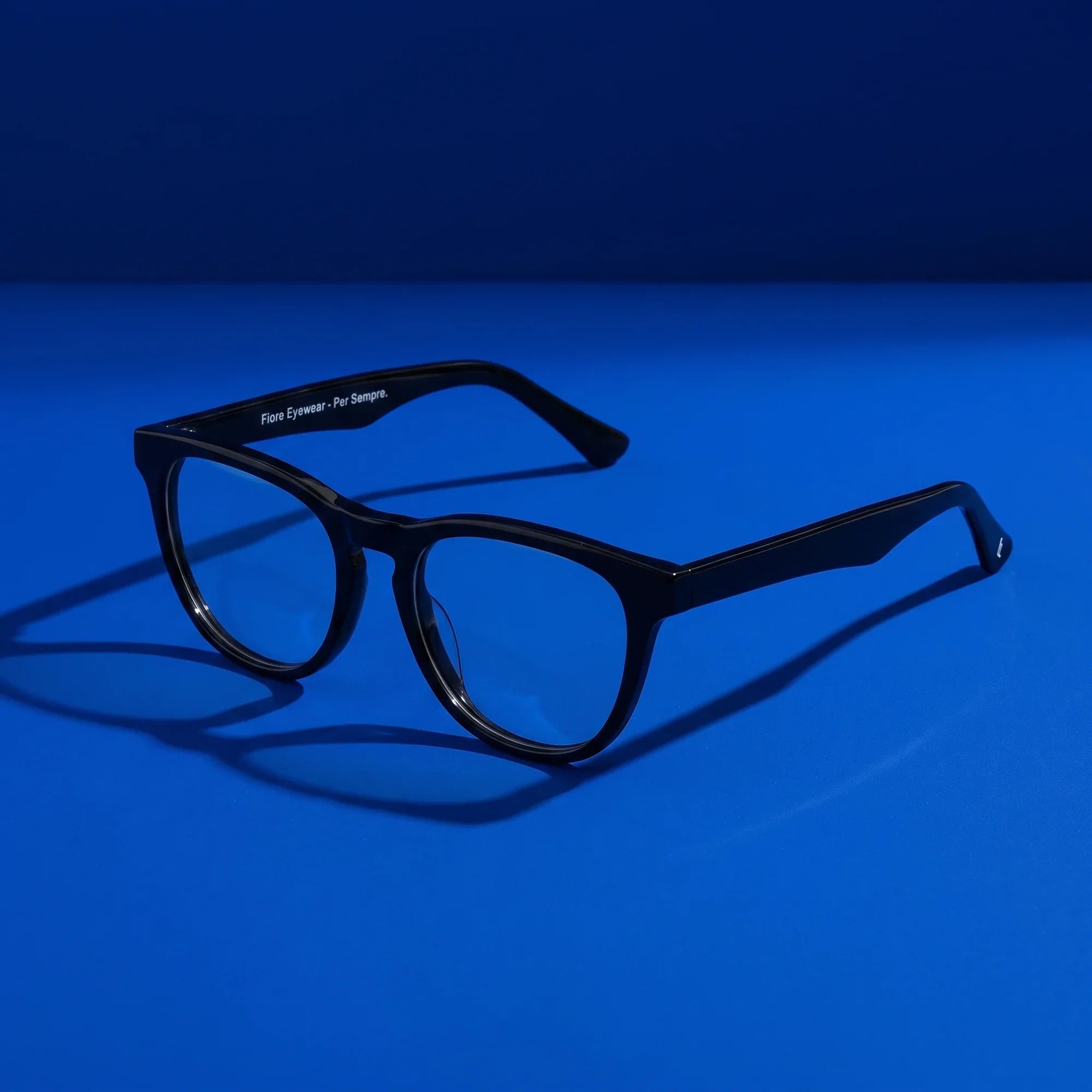 Anteojos Fiore 4488 en negro – hero still life against a deep cobalt backdrop