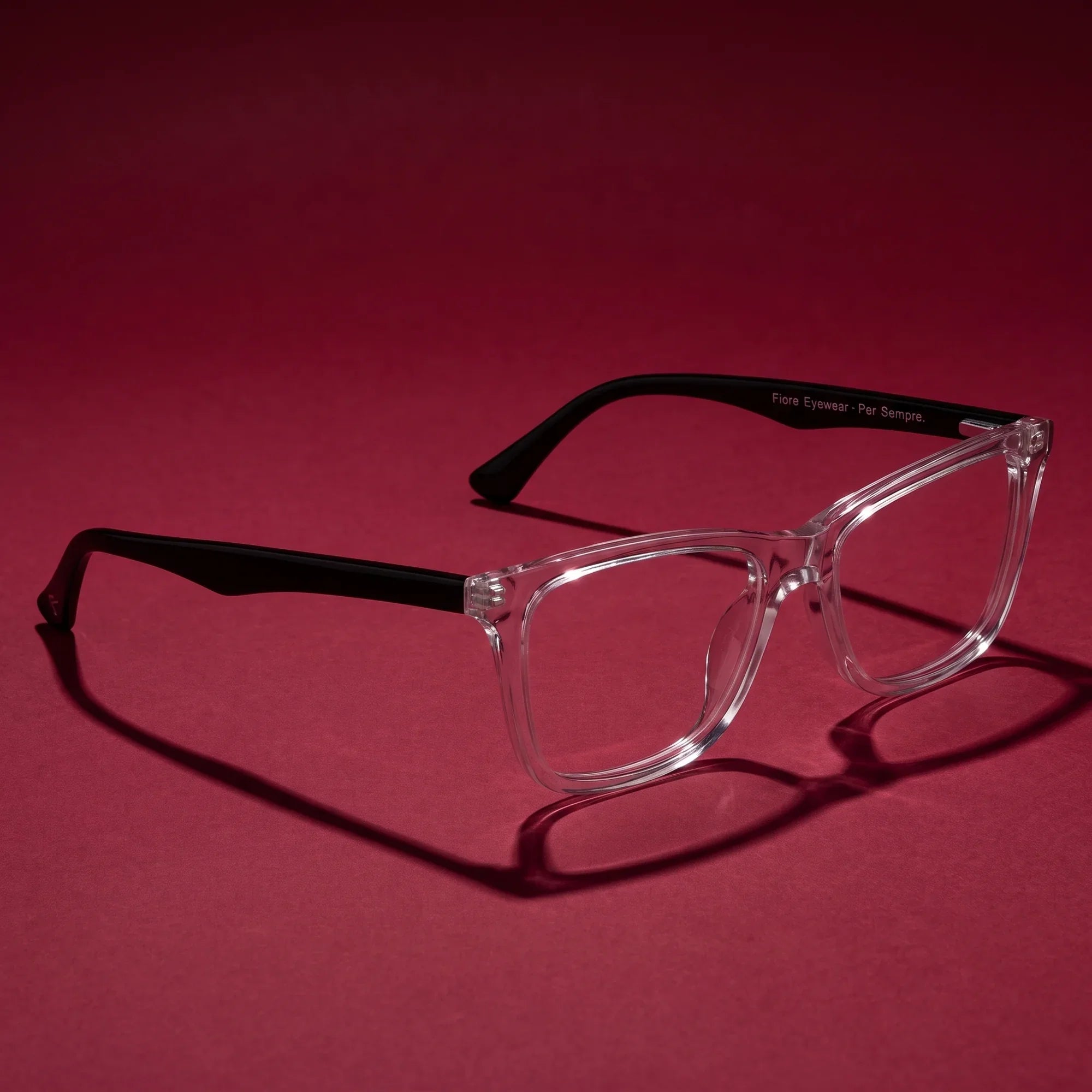 Anteojos Fiore 5228 en transparent – editorial still life on a saturated burgundy set