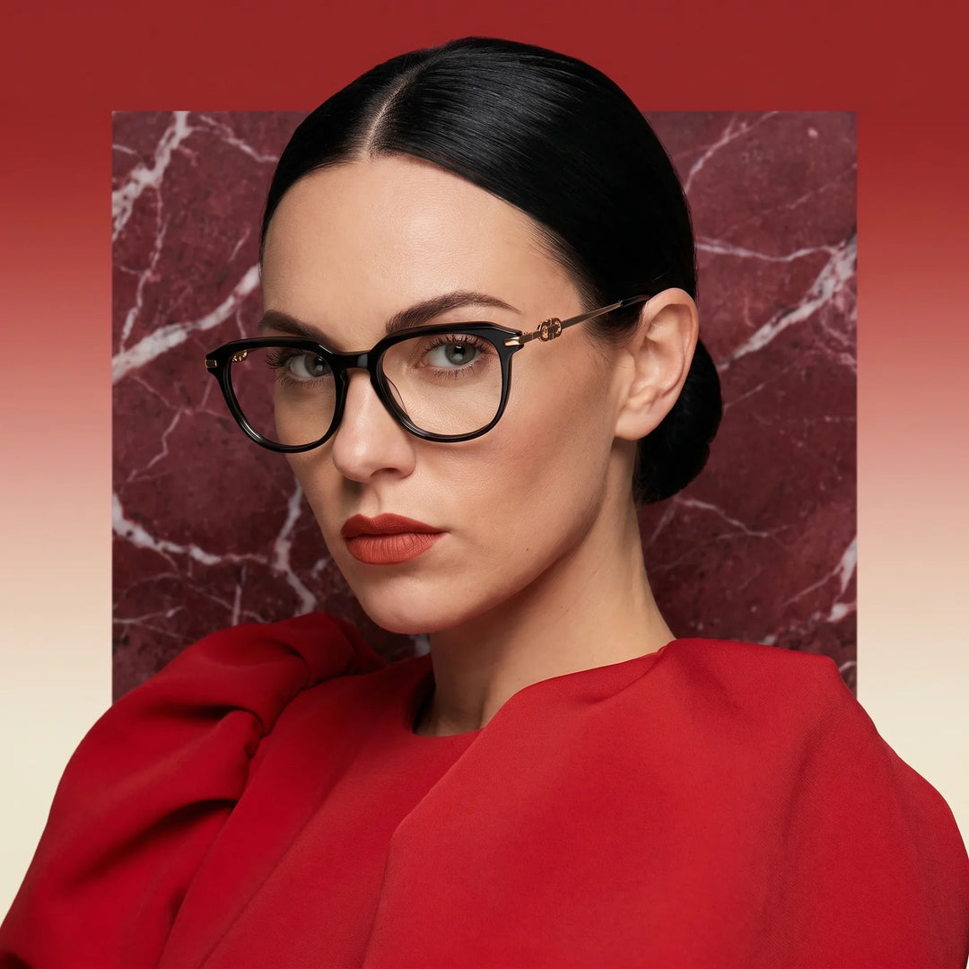 Anteojos Fiore 5409 en negro, en modelo – retrato de campaña, fondo de mármol rojo y vestido escarlata drapeado