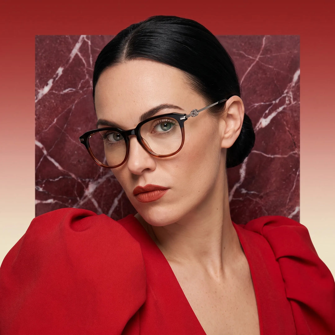 Anteojos Fiore 5409 en black brown, en modelo – retrato de campaña, fondo de mármol rojo y vestido escarlata drapeado