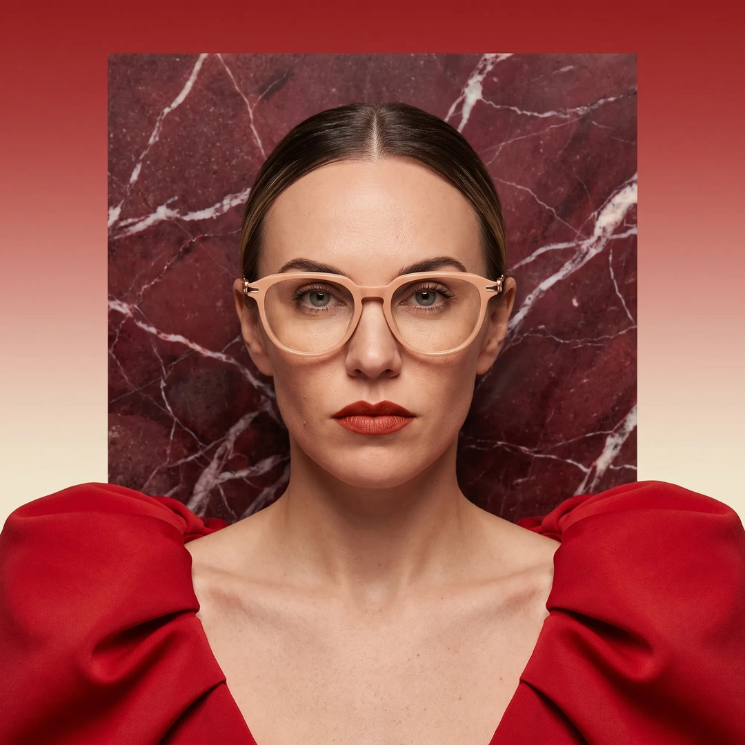 Anteojos Fiore 5409 en milky white, en modelo – retrato de campaña, fondo de mármol rojo y vestido escarlata drapeado