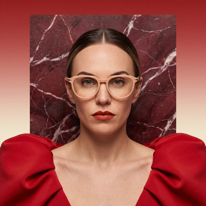 Anteojos Fiore 5409 en milky white, en modelo – retrato de campaña, fondo de mármol rojo y vestido escarlata drapeado