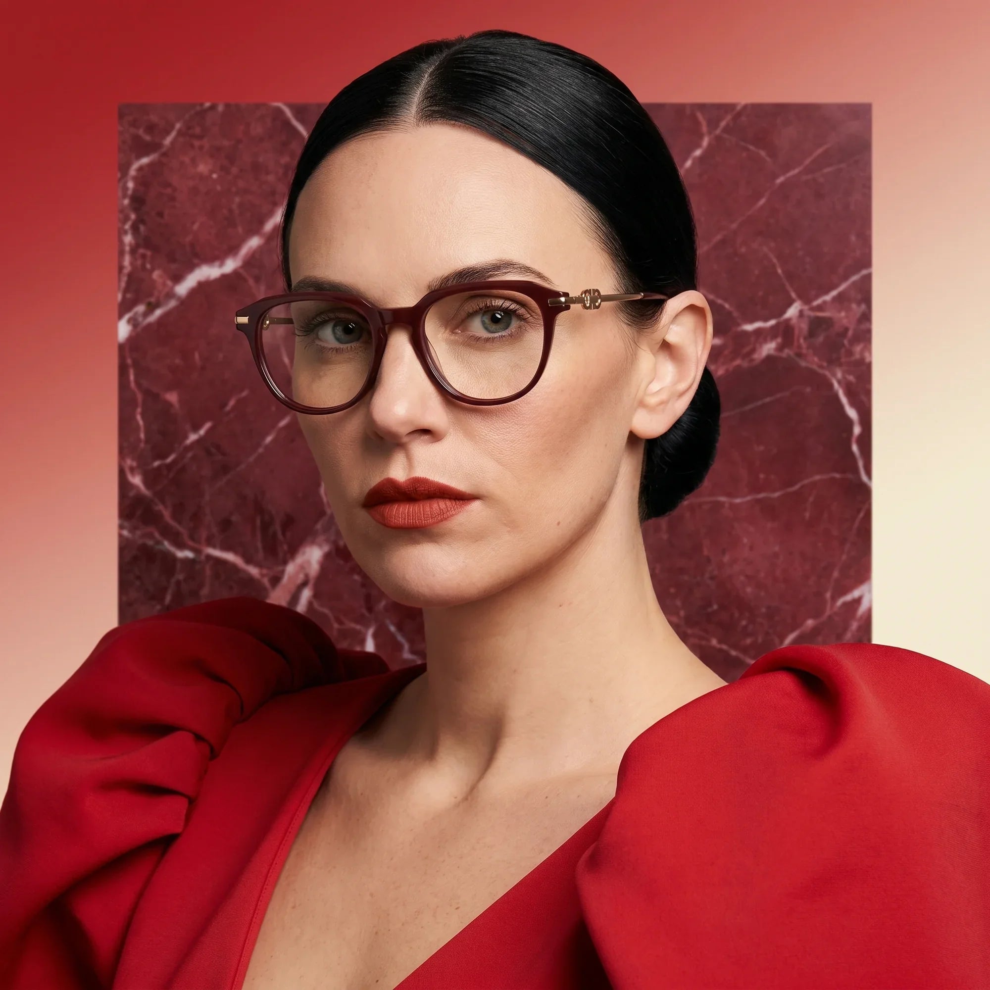 Anteojos Fiore 5409 en brown red, en modelo – retrato de campaña, fondo de mármol rojo y vestido escarlata drapeado