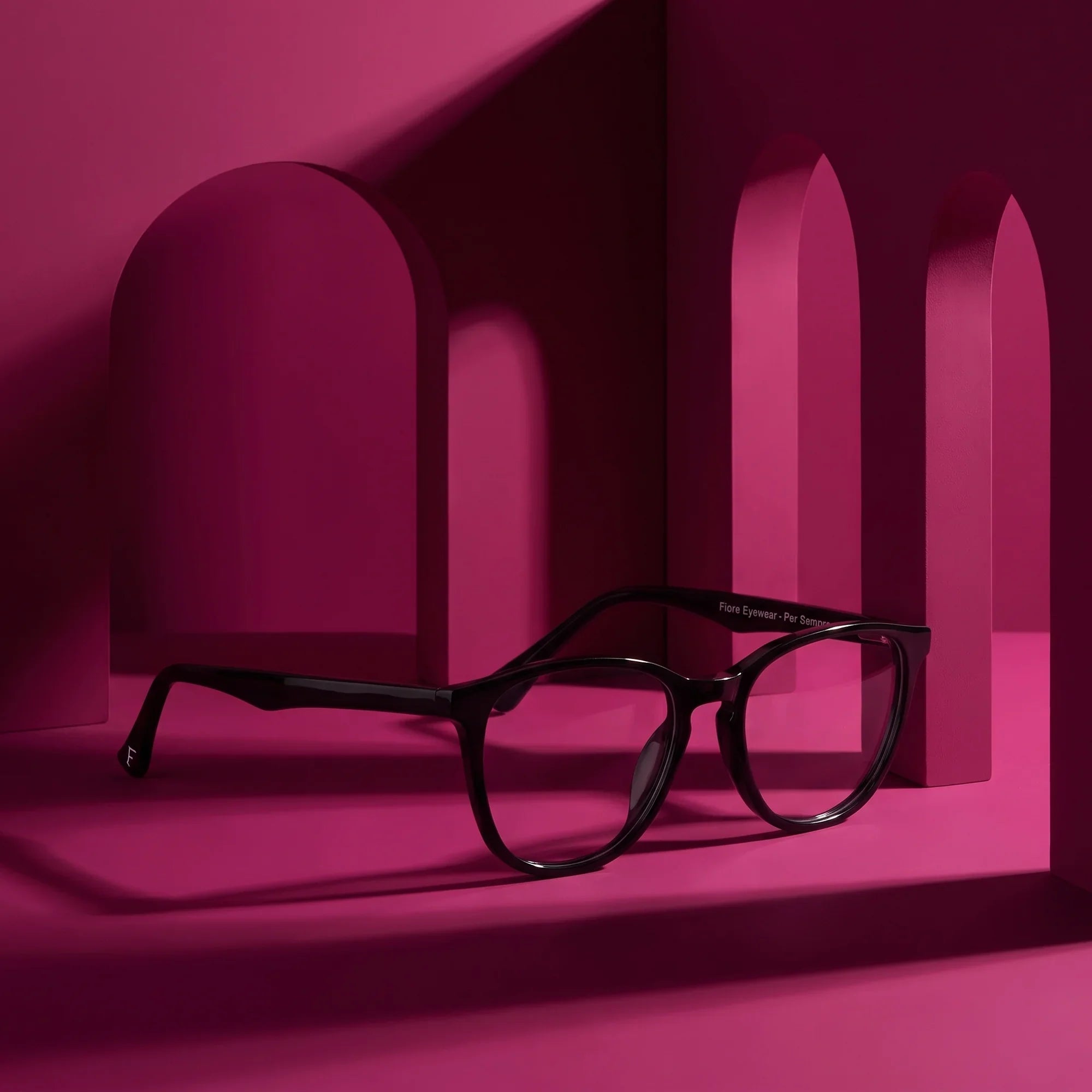 Anteojos Fiore 7046 en negro – staged on a sculptural magenta architecture set