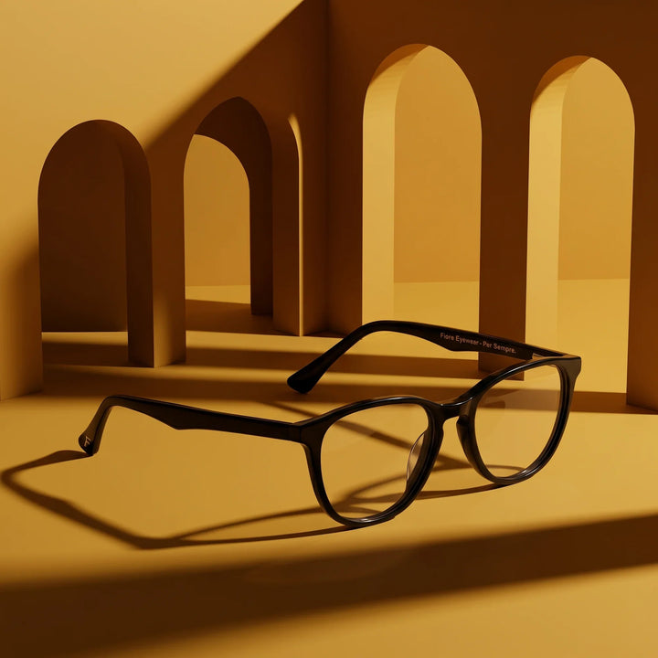 Anteojos Fiore 7046 en negro – displayed on a mustard ochre podium among arches