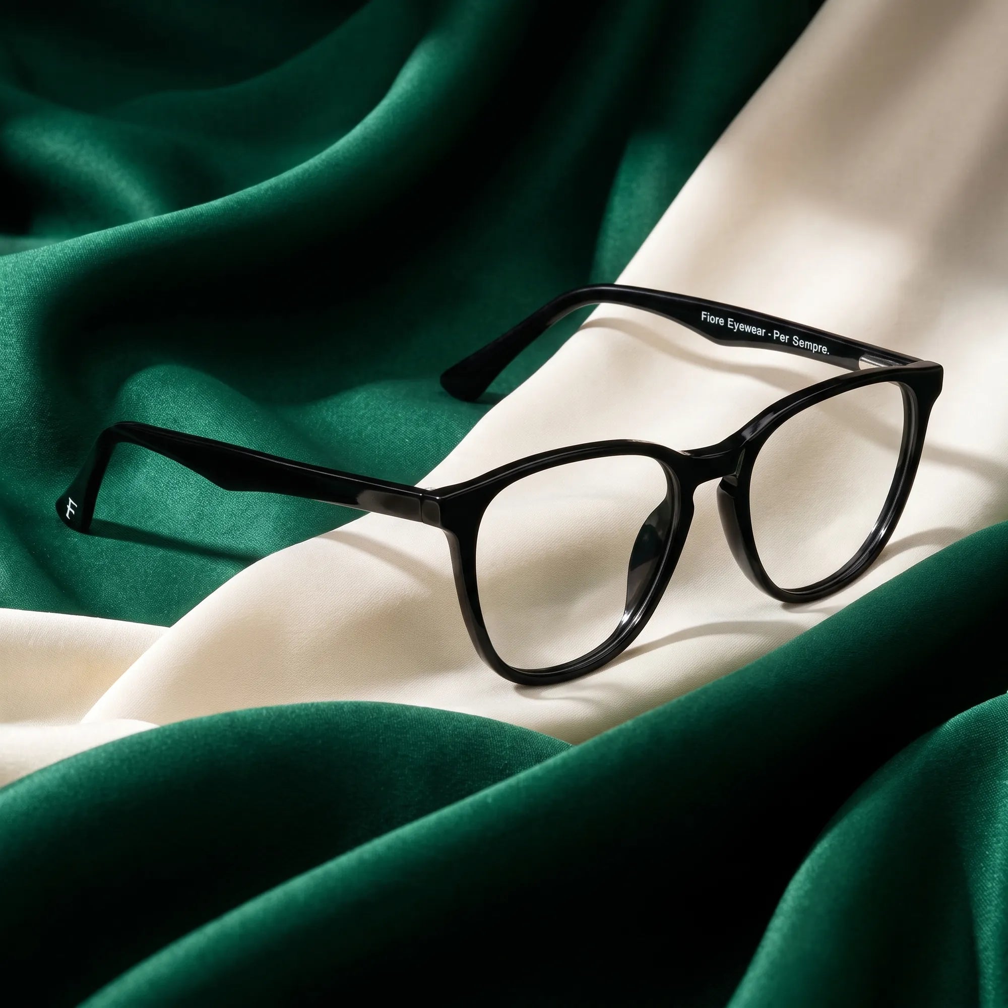 Anteojos Fiore 7046 en negro – resting on draped emerald and ivory silk
