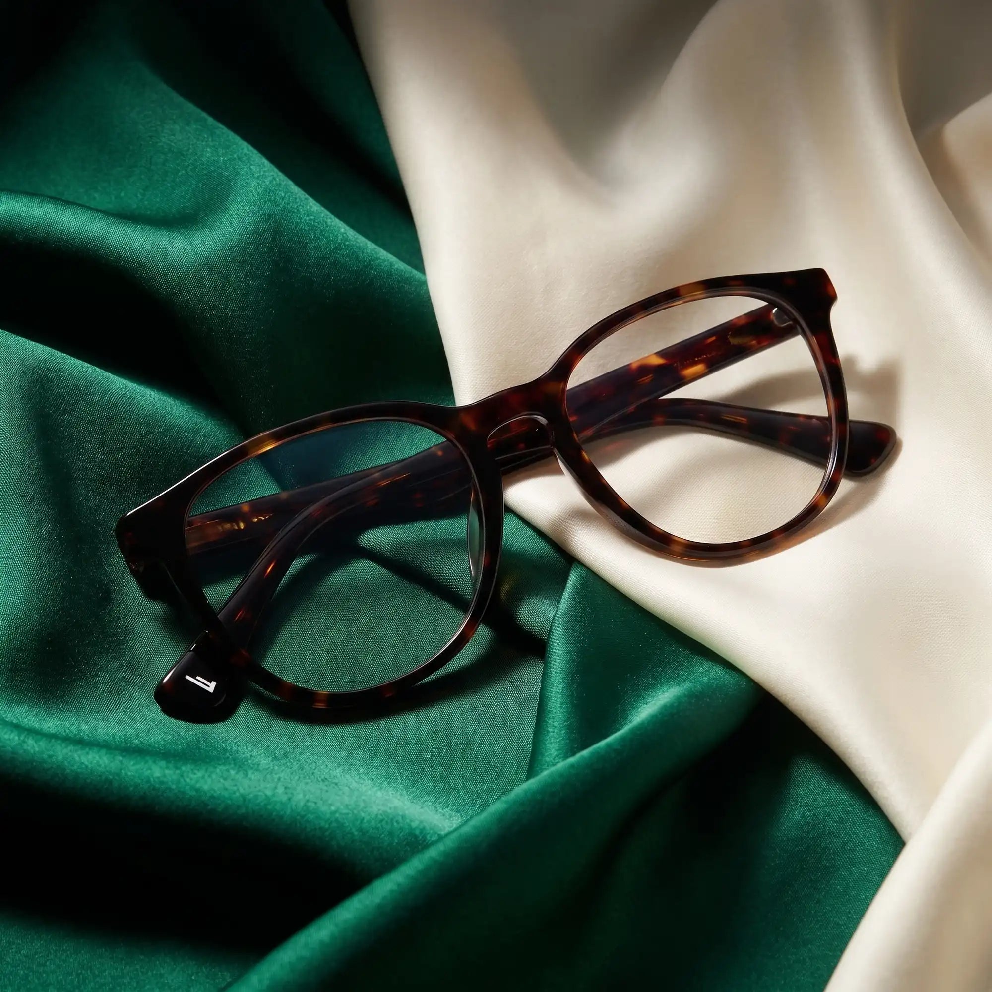 Anteojos Fiore 7046 en tortoiseshell – resting on draped emerald and ivory silk