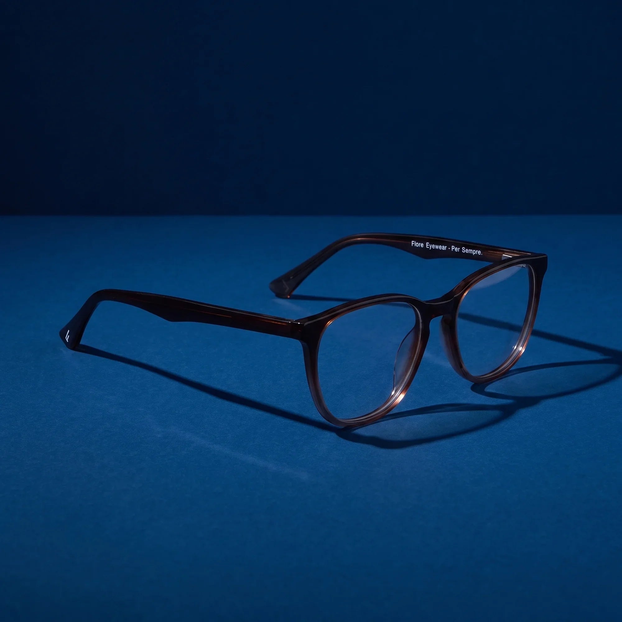 Anteojos Fiore 7046 en gradual brown – hero still life against a deep midnight blue backdrop