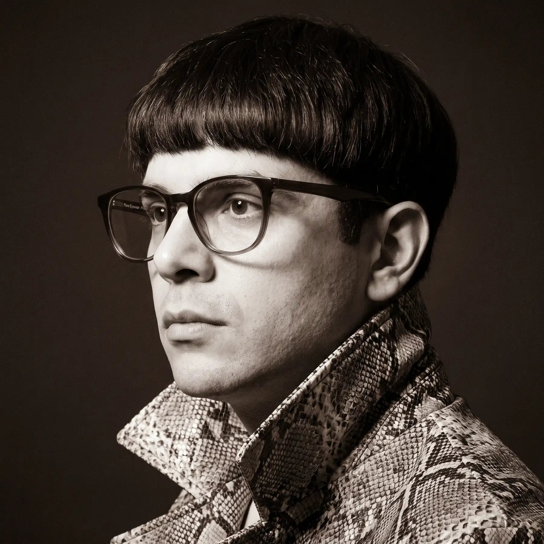 Anteojos Fiore 7046 en gradual brown, en modelo – retrato de campaña, monochrome studio portrait, red graphic accents