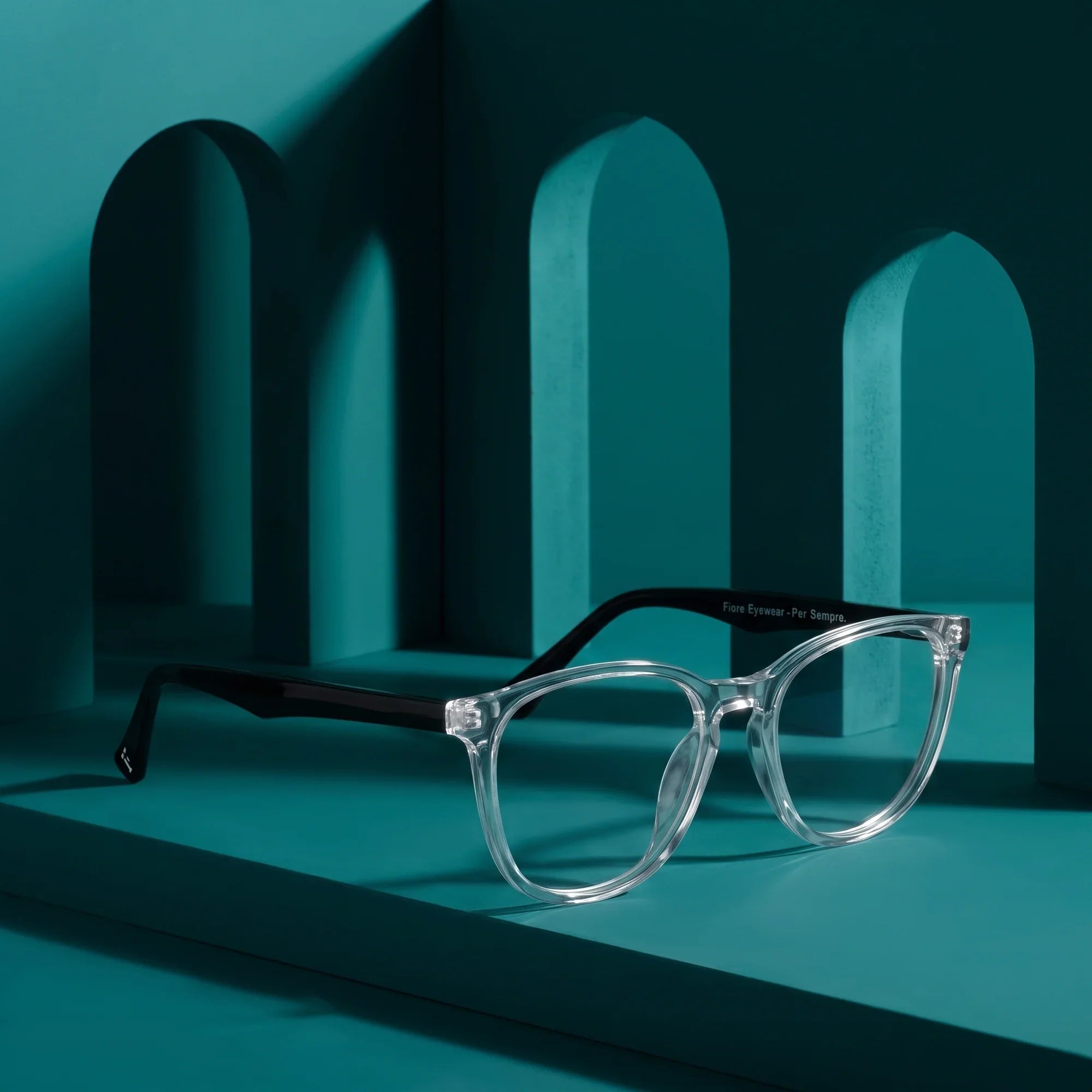 Anteojos Fiore 7046 en transparent – staged on a sculptural teal architecture set