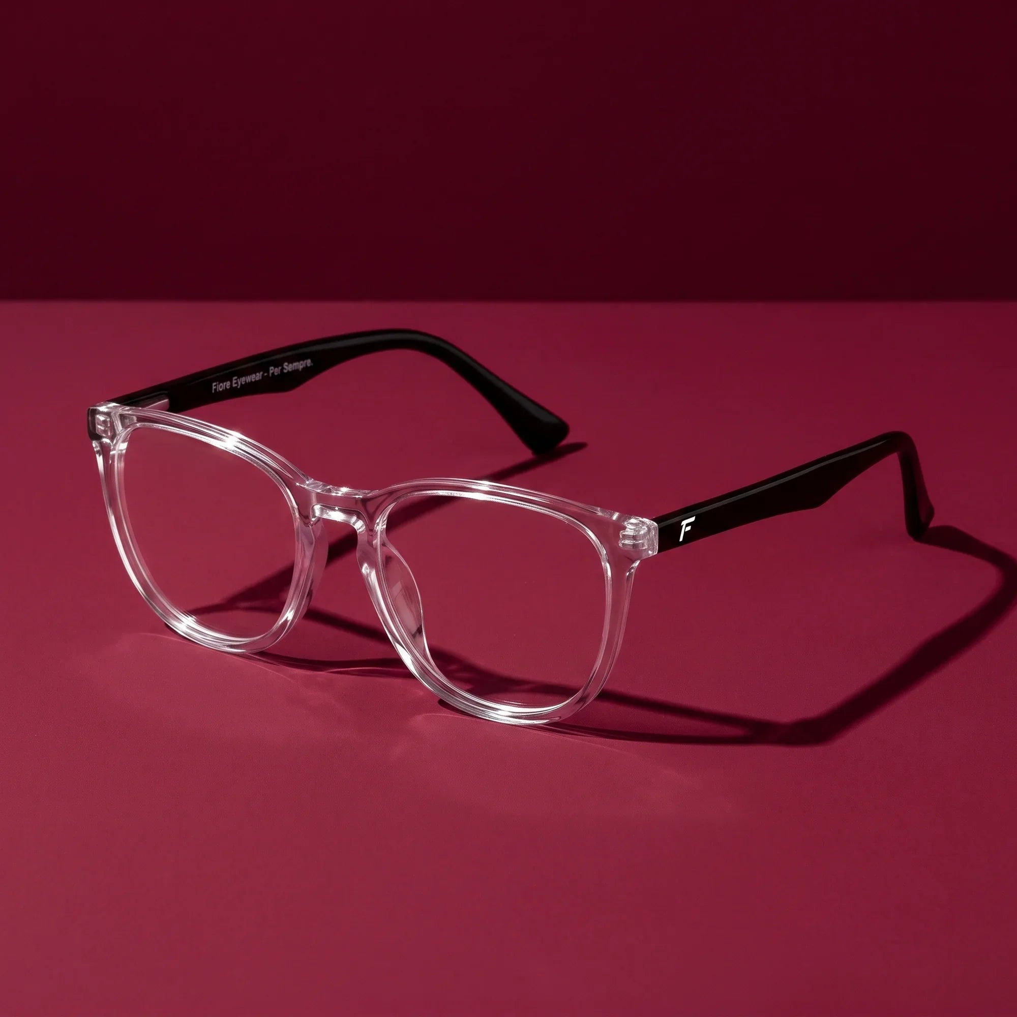 Anteojos Fiore 7046 en transparent – editorial still life on a saturated burgundy set