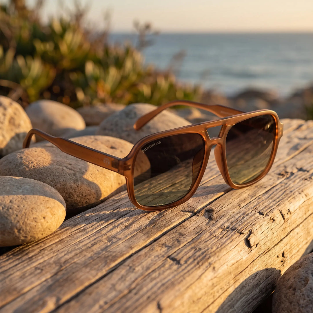 Lentes de sol Bonoboss Orson RPET Brown sobre madera y rocas junto al mar al atardecer #editorial_grid2 #color_brown
