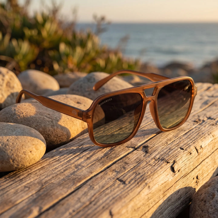 Lentes de sol Bonoboss Orson RPET Brown sobre madera y rocas junto al mar al atardecer #editorial_grid2 #color_brown