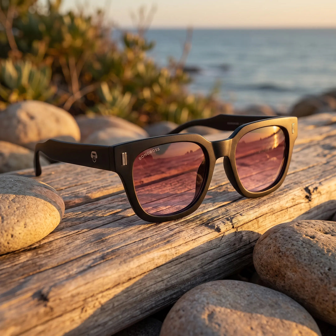 Lentes de sol Bonoboss Osorno RPET Red sobre madera y rocas junto al mar al atardecer #editorial_grid2 #color_red