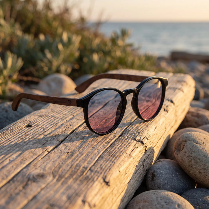 Lentes de sol Bonoboss Paine Pink sobre madera y rocas junto al mar al atardecer #editorial_grid2 #color_pink