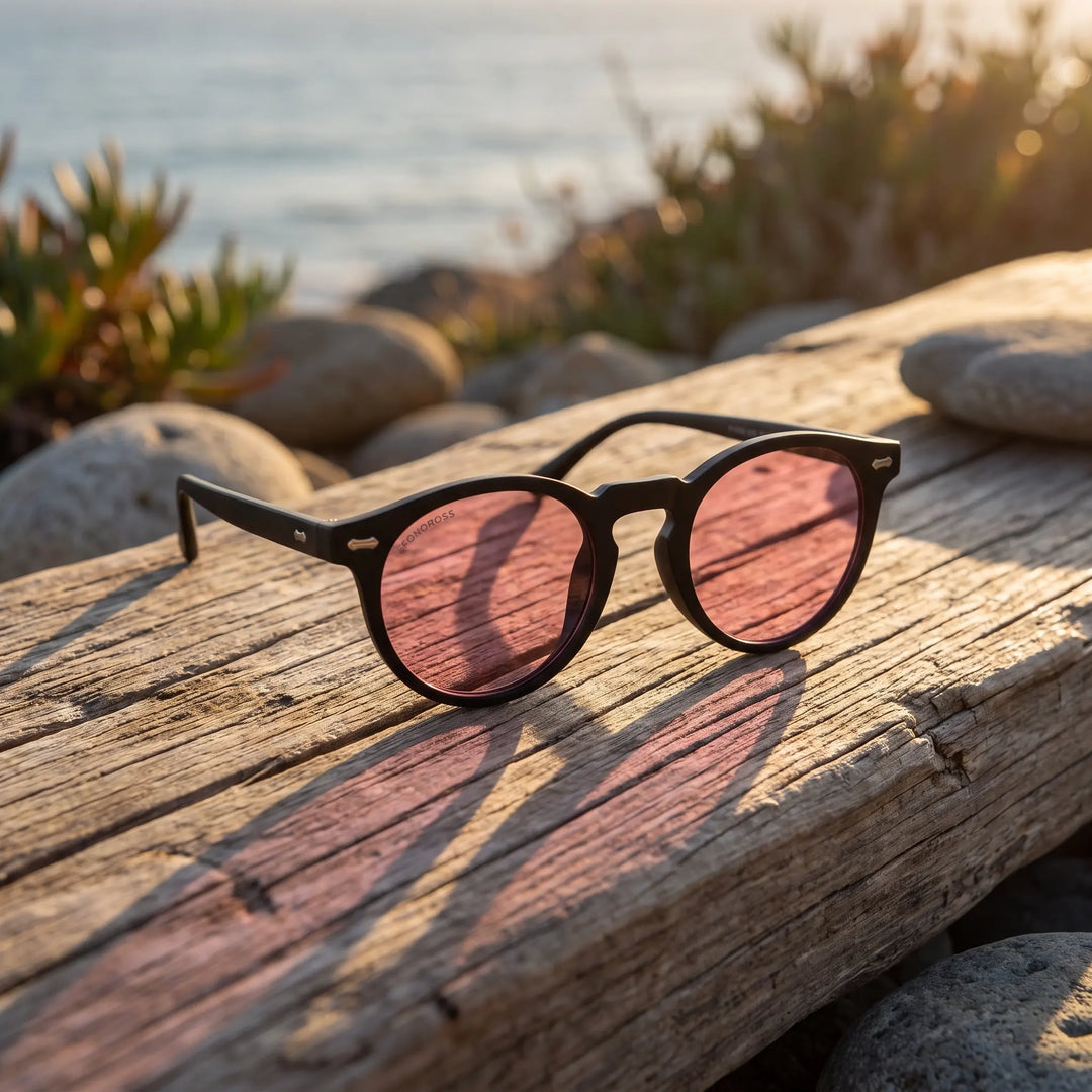 Lentes de sol Bonoboss Temuco RPET Rosado sobre madera y rocas junto al mar al atardecer #editorial_grid2 #color_rosado