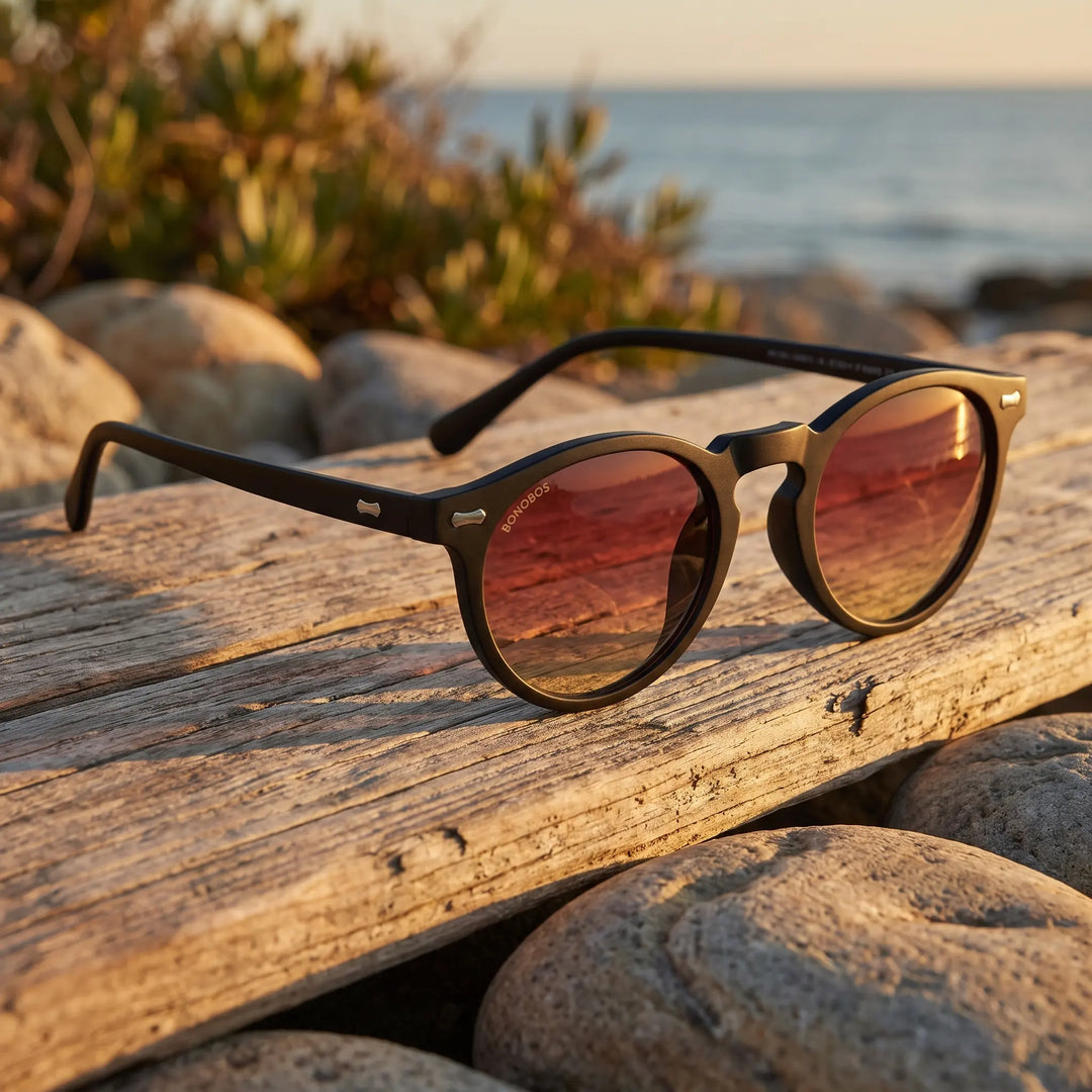 Lentes de sol Bonoboss Temuco RPET Sunset sobre madera y rocas junto al mar al atardecer #editorial_grid2 #color_sunset