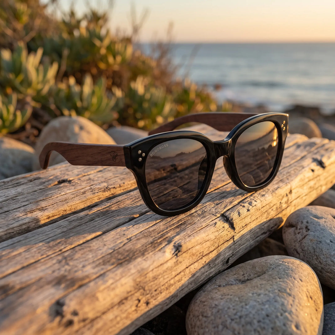 Lentes de sol Bonoboss Tren Tren Negro sobre madera y rocas junto al mar al atardecer #editorial_grid2 #color_negro