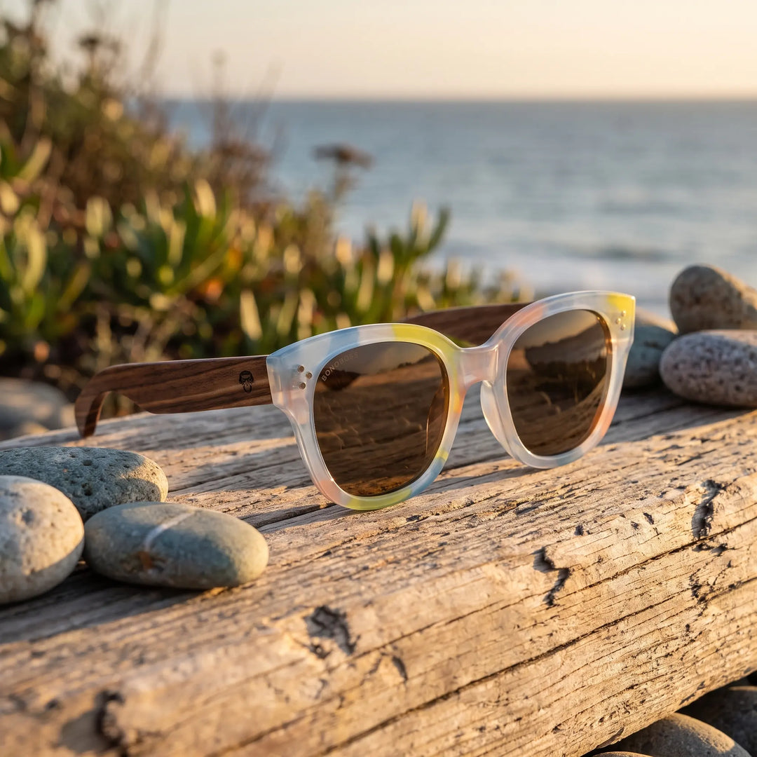 Lentes de sol Bonoboss Tren Tren Yellow sobre madera y rocas junto al mar al atardecer #editorial_grid2 #color_yellow