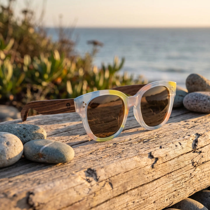 Lentes de sol Bonoboss Tren Tren Yellow sobre madera y rocas junto al mar al atardecer #editorial_grid2 #color_yellow