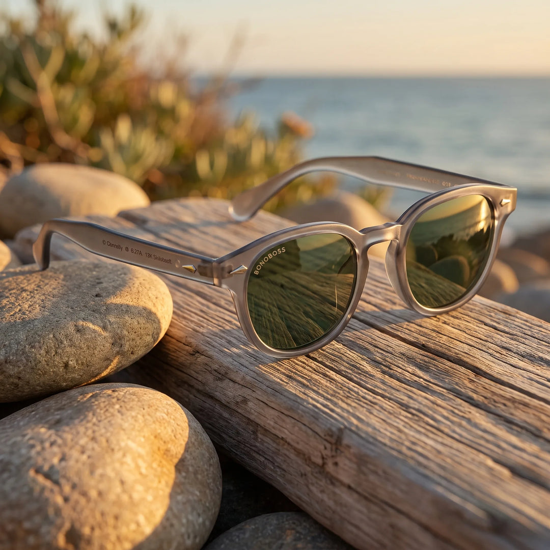 Lentes de sol Bonoboss Waimea RPET Transparente G15 sobre madera y rocas junto al mar al atardecer #editorial_grid2 #color_transparente-g15